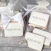 A stack of rectangular butter shortbread cookies with MiRaval logo printed directly on a white, light sugar icing. Some cookies are shown in clear packaging with a twist-tie ribbon bow or inside an organza bag.