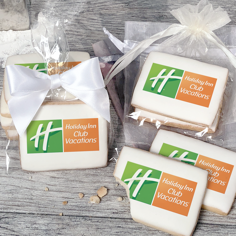 A stack of rectangular butter shortbread cookies with Holiday Inn Club Vacations logo printed directly on a white, light sugar icing. Some cookies are shown in clear packaging with a twist-tie ribbon bow or inside an organza bag.