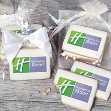 Load image into Gallery viewer, A stack of rectangular butter shortbread cookies with Holiday Inn Resort logo printed directly on a white, light sugar icing. Some cookies are shown in clear packaging with a twist-tie ribbon bow or inside an organza bag.