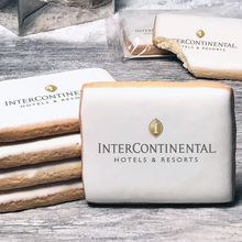 Load image into Gallery viewer, A stack of rectangle butter shortbread cookies with Intercontinental logo printed directly on a white, lemon sugar icing.