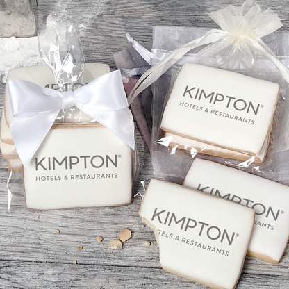 A stack of rectangular butter shortbread cookies with Kimpton logo printed directly on a white, light sugar icing. Some cookies are shown in clear packaging with a twist-tie ribbon bow or inside an organza bag.