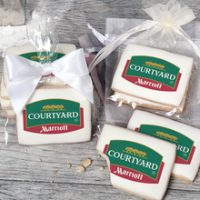 Load image into Gallery viewer, A stack of rectangular butter shortbread cookies with Courtyard logo printed directly on a white, light sugar icing. Some cookies are shown in clear packaging with a twist-tie ribbon bow or inside an organza bag.