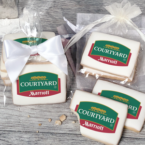 A stack of rectangular butter shortbread cookies with Courtyard logo printed directly on a white, light sugar icing. Some cookies are shown in clear packaging with a twist-tie ribbon bow or inside an organza bag.