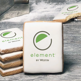 A stack of rectangle butter shortbread cookies with Element by Westin logo printed directly on a white, lemon sugar icing.