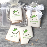 A stack of rectangular butter shortbread cookies with Element by Westin logo printed directly on a white, light sugar icing. Some cookies are shown in clear packaging with a twist-tie ribbon bow or inside an organza bag.