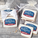 A stack of rectangular butter shortbread cookies with Fairfield Inn & Suites logo printed directly on a white, light sugar icing. Some cookies are shown in clear packaging with a twist-tie ribbon bow or inside an organza bag.
