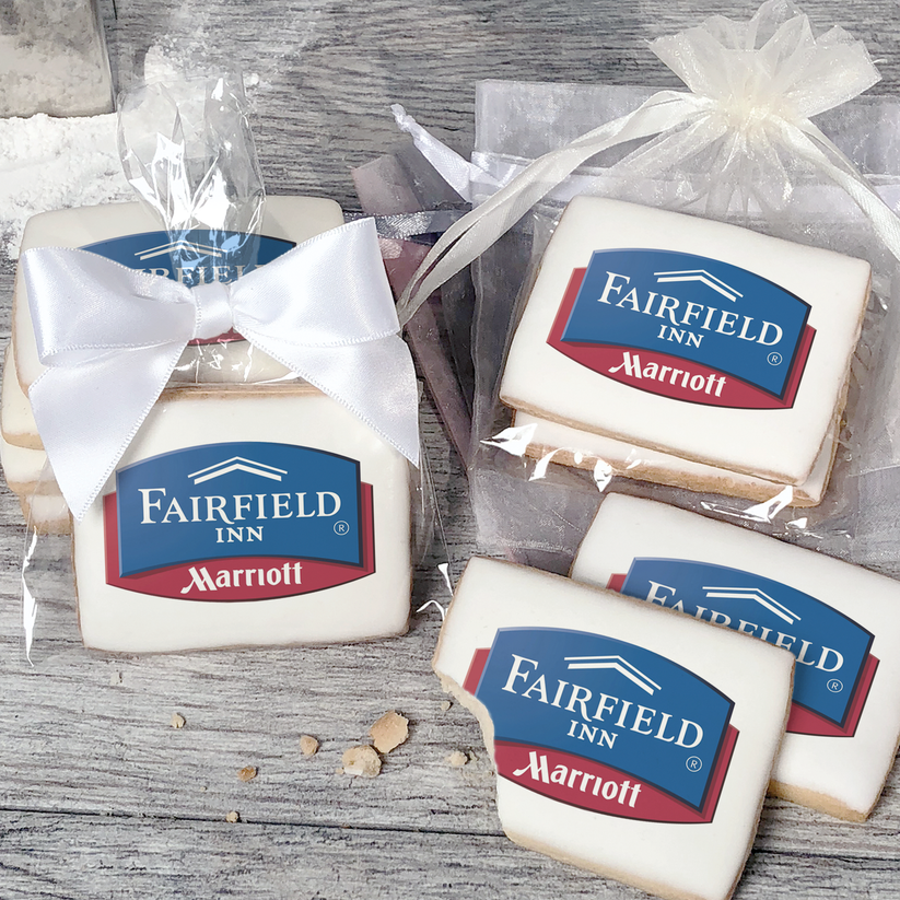 A stack of rectangular butter shortbread cookies with Fairfield Inn & Suites logo printed directly on a white, light sugar icing. Some cookies are shown in clear packaging with a twist-tie ribbon bow or inside an organza bag.