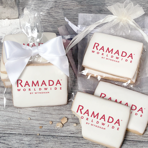 A stack of rectangular butter shortbread cookies with Ramada Worldwide logo printed directly on a white, light sugar icing. Some cookies are shown in clear packaging with a twist-tie ribbon bow or inside an organza bag.