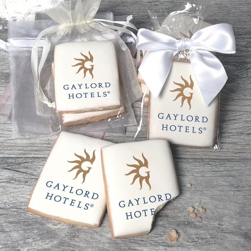 A stack of rectangular butter shortbread cookies with Gaylord Hotels logo printed directly on a white, light sugar icing. Some cookies are shown in clear packaging with a twist-tie ribbon bow or inside an organza bag.