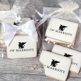A stack of rectangular butter shortbread cookies with JW Marriott logo printed directly on a white, light sugar icing. Some cookies are shown in clear packaging with a twist-tie ribbon bow or inside an organza bag.