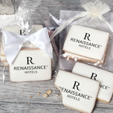 A stack of rectangular butter shortbread cookies with Renaissance logo printed directly on a white, light sugar icing. Some cookies are shown in clear packaging with a twist-tie ribbon bow or inside an organza bag.