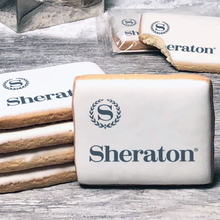 Load image into Gallery viewer, A stack of rectangle butter shortbread cookies with Sheraton logo printed directly on a white, lemon sugar icing.
