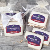 A stack of rectangular butter shortbread cookies with Springhill Suites logo printed directly on a white, light sugar icing. Some cookies are shown in clear packaging with a twist-tie ribbon bow or inside an organza bag.