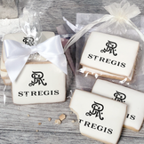 A stack of rectangular butter shortbread cookies with St Regis logo printed directly on a white, light sugar icing. Some cookies are shown in clear packaging with a twist-tie ribbon bow or inside an organza bag.