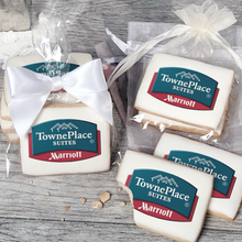 Load image into Gallery viewer, A stack of rectangular butter shortbread cookies with Towneplace Suites logo printed directly on a white, light sugar icing. Some cookies are shown in clear packaging with a twist-tie ribbon bow or inside an organza bag.
