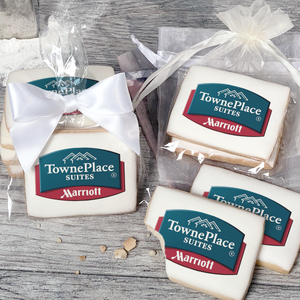 A stack of rectangular butter shortbread cookies with Towneplace Suites logo printed directly on a white, light sugar icing. Some cookies are shown in clear packaging with a twist-tie ribbon bow or inside an organza bag.