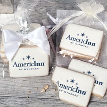 Load image into Gallery viewer, A stack of rectangular butter shortbread cookies with AmericInn logo printed directly on a white, light sugar icing. Some cookies are shown in clear packaging with a twist-tie ribbon bow or inside an organza bag.