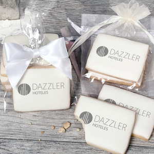 A stack of rectangular butter shortbread cookies with Dazzler logo printed directly on a white, light sugar icing. Some cookies are shown in clear packaging with a twist-tie ribbon bow or inside an organza bag.