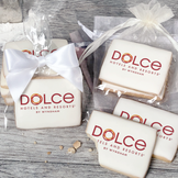 A stack of rectangular butter shortbread cookies with Dolce Hotels & Resorts logo printed directly on a white, light sugar icing. Some cookies are shown in clear packaging with a twist-tie ribbon bow or inside an organza bag.