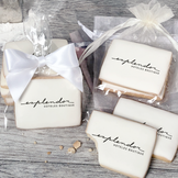 A stack of rectangular butter shortbread cookies with Esplendor logo printed directly on a white, light sugar icing. Some cookies are shown in clear packaging with a twist-tie ribbon bow or inside an organza bag.