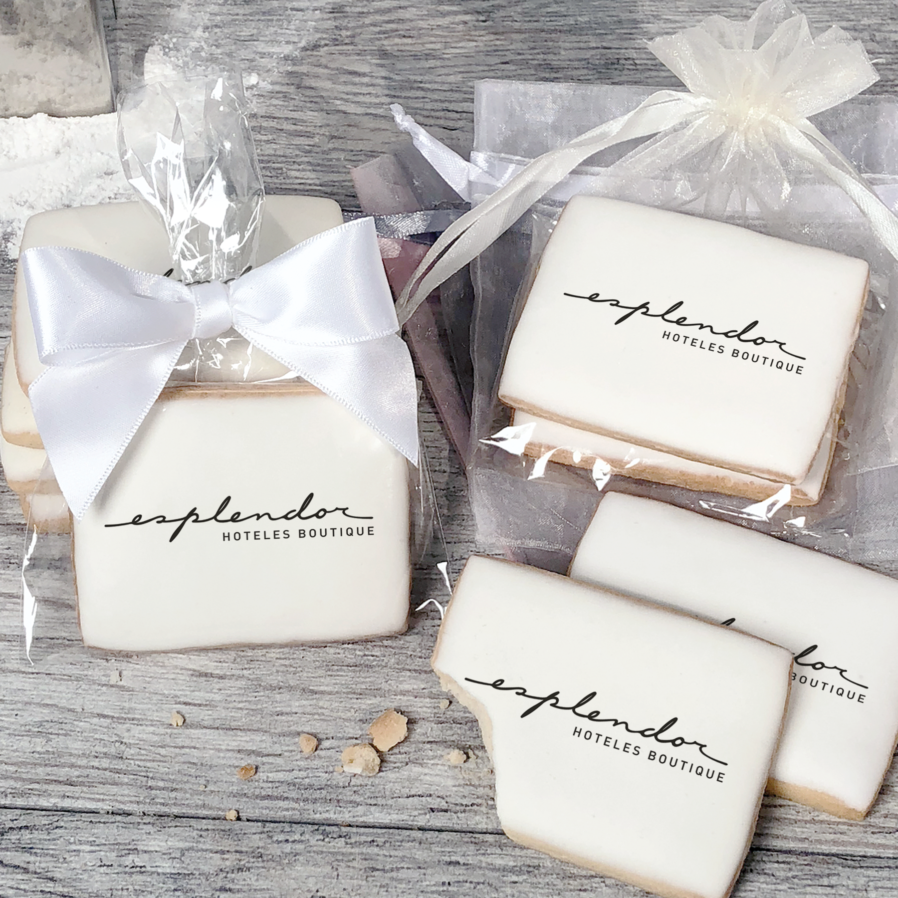 A stack of rectangular butter shortbread cookies with Esplendor logo printed directly on a white, light sugar icing. Some cookies are shown in clear packaging with a twist-tie ribbon bow or inside an organza bag.