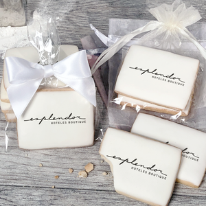 A stack of rectangular butter shortbread cookies with Esplendor logo printed directly on a white, light sugar icing. Some cookies are shown in clear packaging with a twist-tie ribbon bow or inside an organza bag.