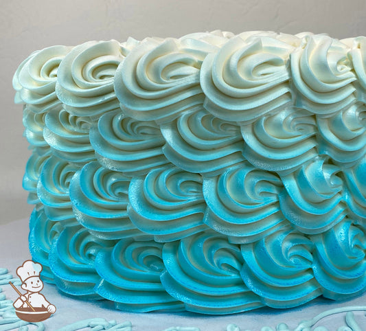Single tier cake with white icing, decorated with buttercream rosettes and an added light-blue Ombre color.