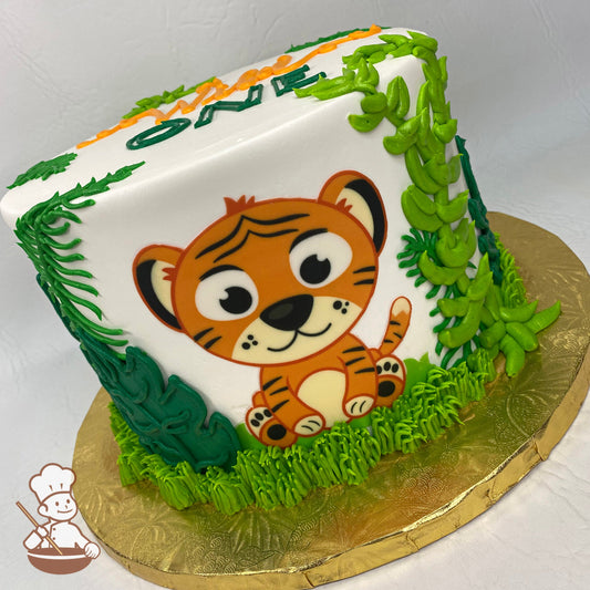 Single tier cake with smooth white icing, decorated with a printed baby-tiger in front of the cake and buttercream green jungle leaves.