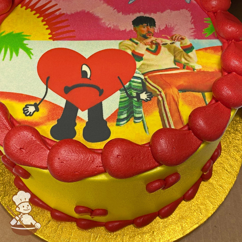 Single tier cake with smooth yellow icing and buttercream red hearts on the cake wall and a printed image of bad bunny on top.