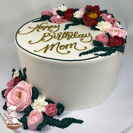 Single tier cake with white icing, decorated with burgundy, pink, light-pink and white buttercream flowers and a custom message in gold color.