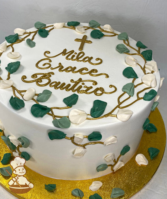 Single tier cake with smooth white icing and decorated with buttercream foliage, piped royal icing gold vines and a gold cross.