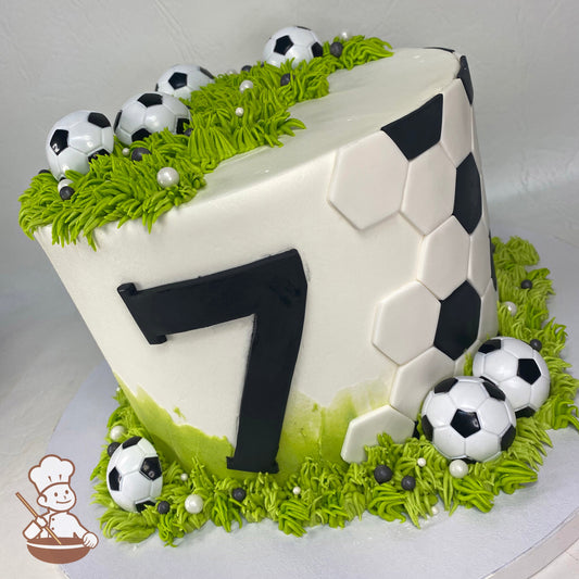 Cake decorated with fondant hexagon patterns to imitate a soccer ball. The cake also has green buttercream grass and plastic soccer ball rings.