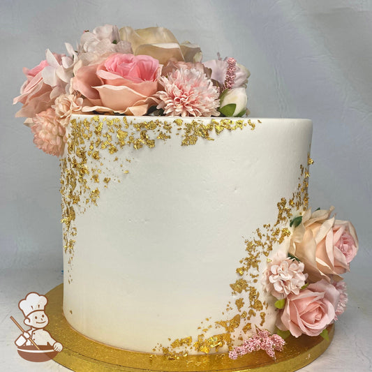 Single tier cake with smooth white icing and decorated with pastel-pink silk flowers and gold flakes on the cake walls.