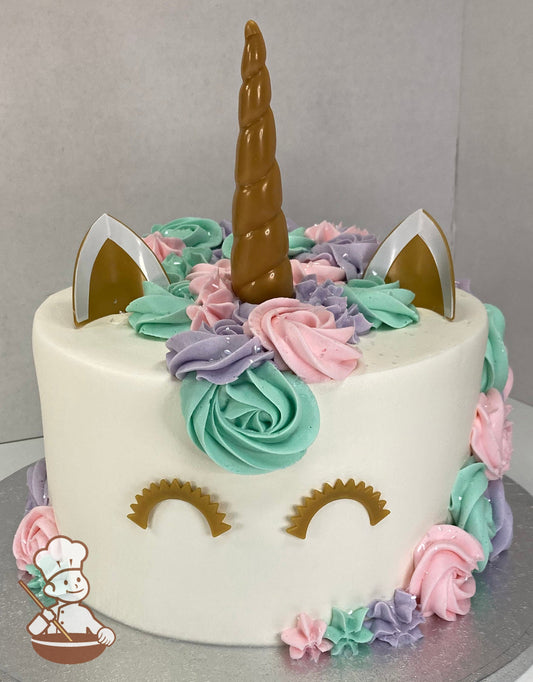 Cake decorated to look like a unicorn with a plastic horn, ears and eyes. The cake also has buttercream rosettes for the mane in pastel colors.