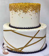 2-tier round cake with gold sprinkles on the top tier cascading down the walls and a gold ribbon on the cake walls of the bottom tier.