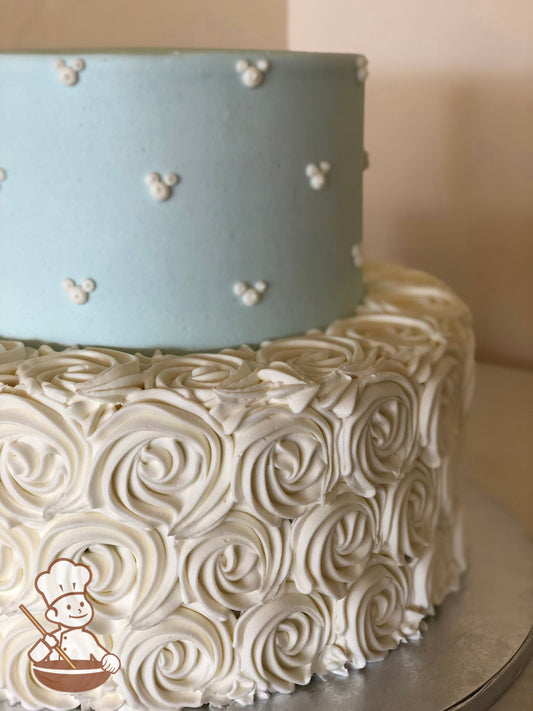 2-tier cake with light blue icing on the top tier with three dot arrangement to look like Mickey's head and white rosettes on the bottom tier.