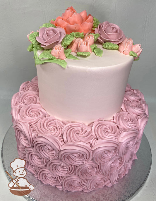 2-tier cake with pink rosettes on the bottom tier and pink icing on the top tier with buttercream peonies and roses as the topper.