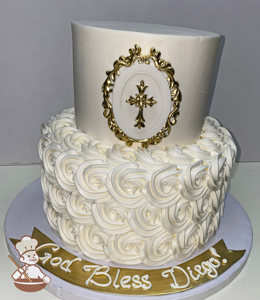 2-tier cake with white buttercream rosettes on the bottom tier and smooth white icing and a gold fondant cross on the top tier cake wall.