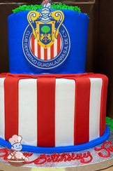 2-tier cake with white icing and red fondant stripes on the bottom tier. The top tier has blue icing and the Chivas logo in the front center.