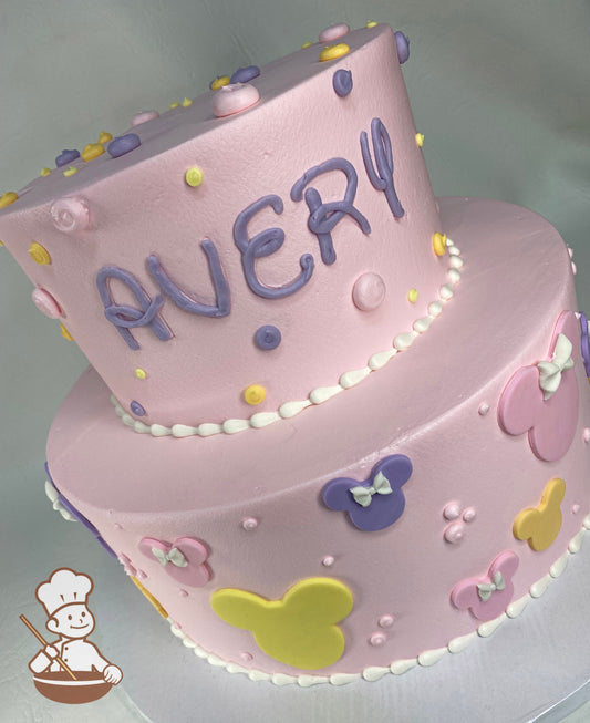 2-tier cake with smooth pink icing and decorated with yellow, purple and pink fondant Minnie Mouse silhouettes with small fondant bows.