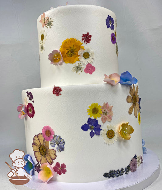 2-tier cake with smooth white icing and decorated with dried pressed flowers all over and touches of fondant blossoms in a varitey of colors.