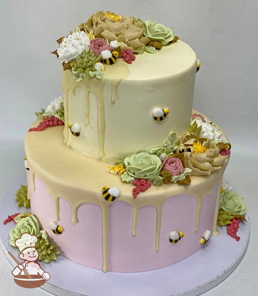 Cake decorated with pink icing on the bottom tier and yellow icing on the top tier. The cake also has buttercream flowers, bees and yellow drip.