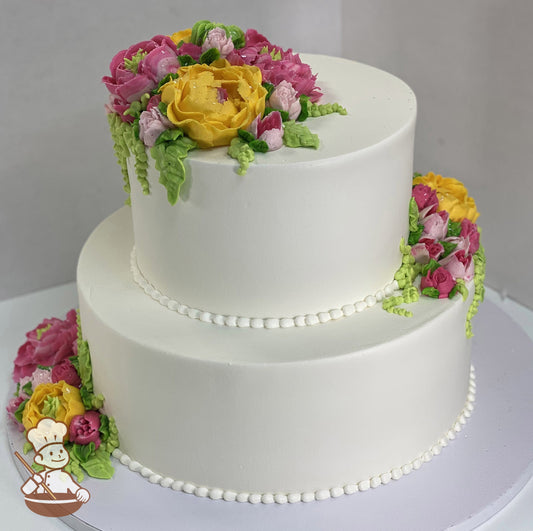 2-tier cake with smooth white icing and decorated with buttercream flowers in hot-pink, yellow and blush-pink colors.