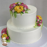 2-tier cake with smooth white icing and decorated with buttercream flowers in hot-pink, yellow and blush-pink colors.