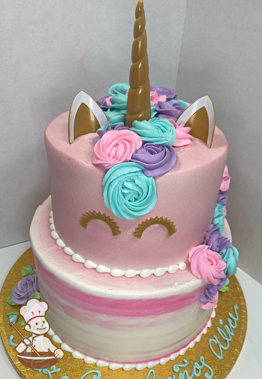 Cake with a pink and white watercolor texture on the bottom tier and the top tier has pink icing and a plastic gold horn, ears and eyes.