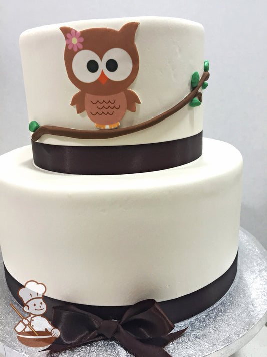 2-tier cake with smooth white icing and decorated with a printed owl on the top tier and a buttercream branch.