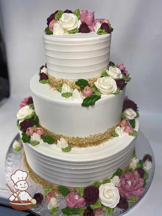 3-tier cake with a horizontal texture on alternating tiers, all tiers have gold sugar and buttercream flowers in pink & burgundy colors.