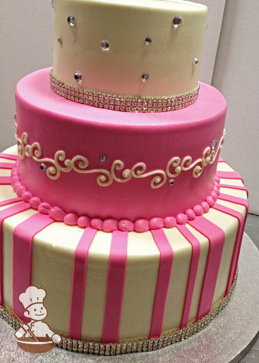 3-tier cake with white and pink icing, and decorated with hot pink fondant stripes, white buttercream scrolls and a rhinestone band.