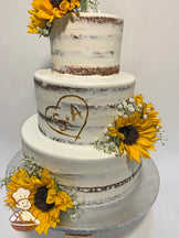 Cake with white icing, decorated with a scraped texture to show some of the cake, silk sunflowers, fake baby's breath and a buttercream heart.
