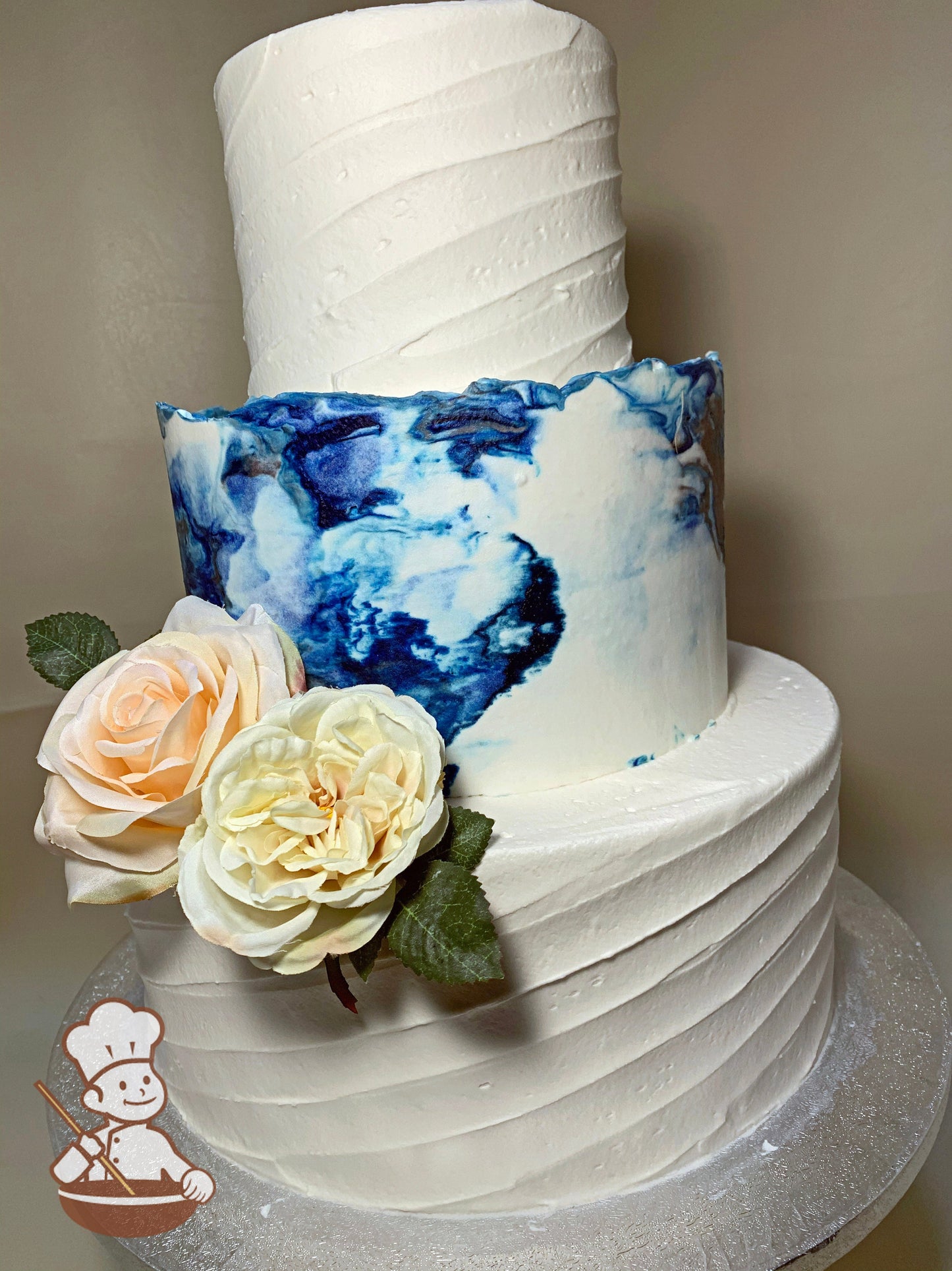 3-tier cake with decorated with a diagonal angle texture on the bottom and top tier, and the middle tier has a blue marble buttercream texture.
